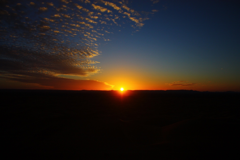 サハラ砂漠から見る、地平線に沈む夕日の画像です。